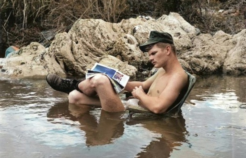 US soldier reading a magazine while sitting in a river